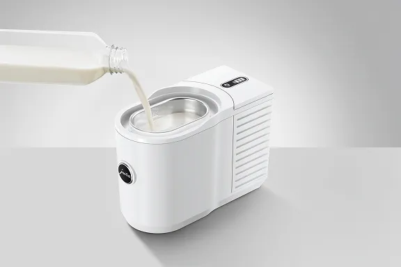 Weißer JURA-Milchkühler (Cool Control) mit herausnehmbarem Edelstahlbehälter; Milch wird aus einer Flasche in den Behälter gegossen.