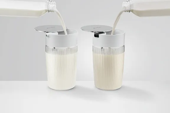 Zwei geriffelte JURA-Glasbehälter mit verchromten Deckeln und Ausguss; beide werden gleichzeitig mit Milch befüllt.